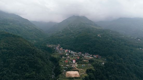 Aerial view of a misty valley town surrounded by lush green hills and cloud-covered mountain peaks.