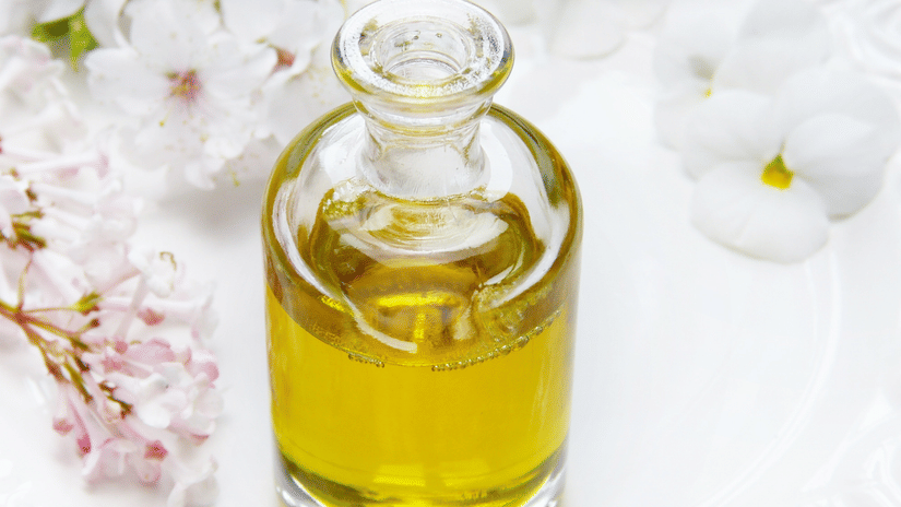 A close up of a glass bottle with ayurvedic essential oil and flower petals next to it.