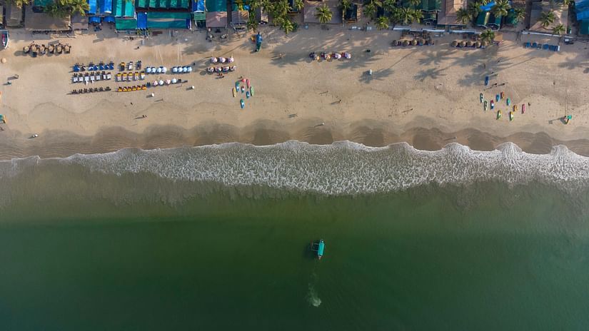 A top-down view of the serene Candolim beach featuring shacks, sun loungers, and a boat docked in the water.