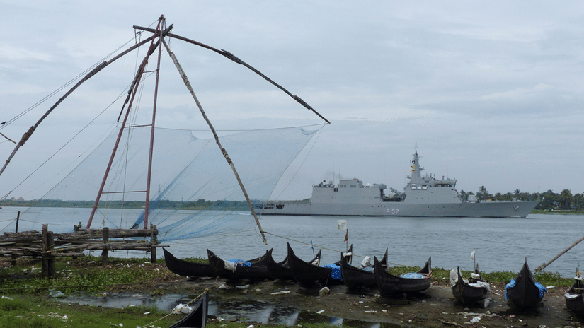 Chinese fishing nets under a cloudy sky in Fort Kochi with boats lined up and a ship sailing on the water