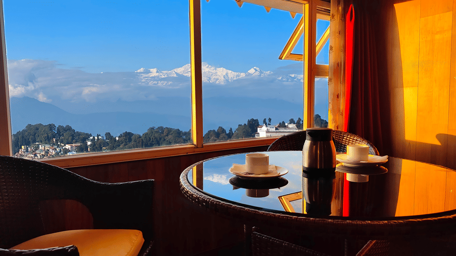 Panoramic window view with seating area and hillside scenery at Mount Thistle Boutique Hotel, Darjeeling.