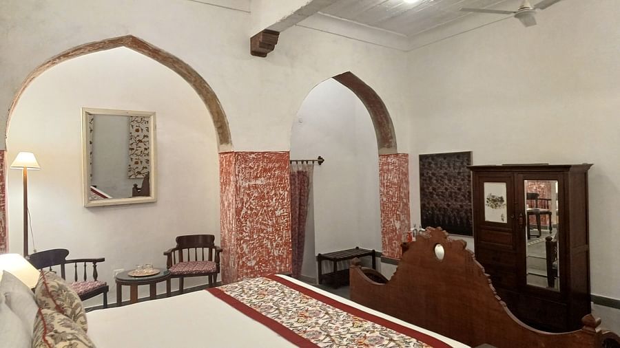 Ornate bedroom with carved wooden bed and authentic heritage furnishings in historic Neemrana Fort-Palace setting.