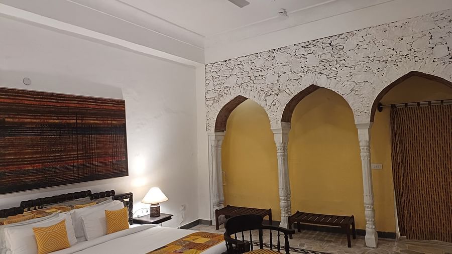 Heritage hotel room with decorative arched alcoves, traditional wooden furniture, white walls, ceiling fan, and authentic fort palace architectural details.