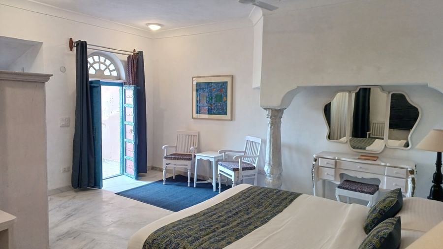 Bright room with white bed, patterned runners, arched doorway, blue accents, and ceiling fan at Neemrana Fort-Palace - 15th Century, Delhi-Jaipur Highway.