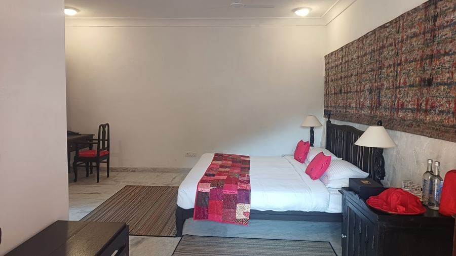 Large bedroom with black bed frame, pink accent pillows, textured wall art, and work desk at Neemrana Fort-Palace - 15th Century, Delhi-Jaipur Highway.