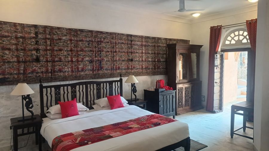 Heritage suite with ornate black headboard, antique cabinet, large tapestry, and arched doorway at Neemrana Fort-Palace - 15th Century, Delhi-Jaipur Highway.