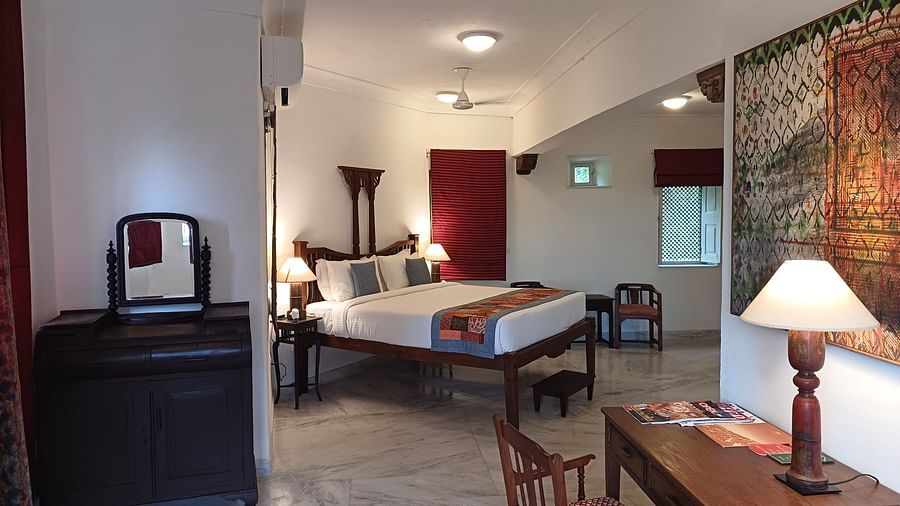Bedroom with dark wooden bed, carved cabinet, and traditional artwork at Neemrana Fort-Palace.