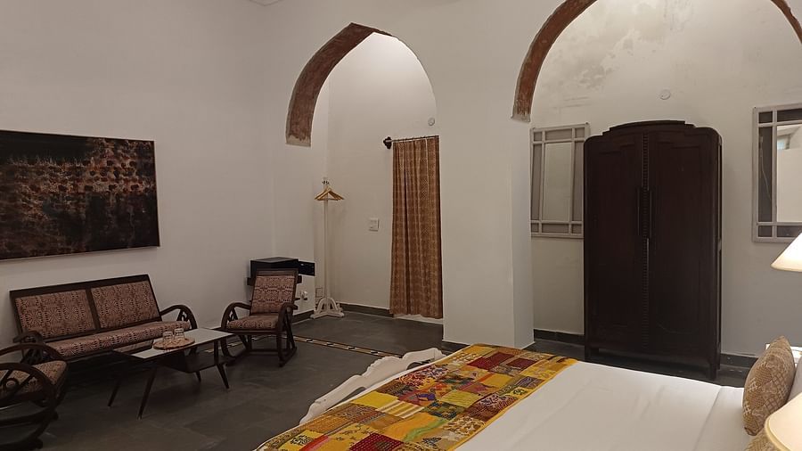 Spacious heritage hotel room with arched doorways, traditional wooden furniture, colorful bedding, and whitewashed walls showcasing 15th-century architecture.