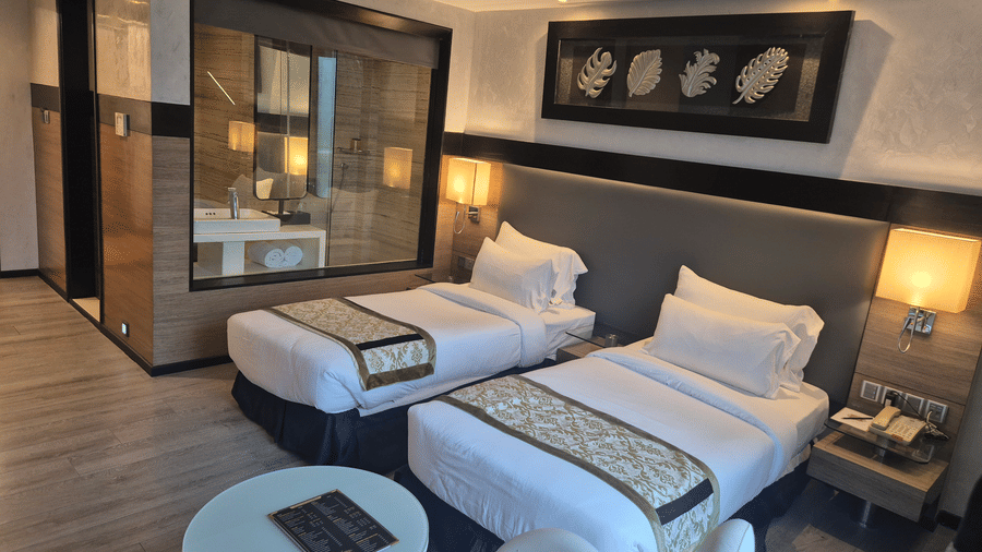 Modern hotel room featuring twin beds with decorative runners, warm lighting, and a view into the bathroom.