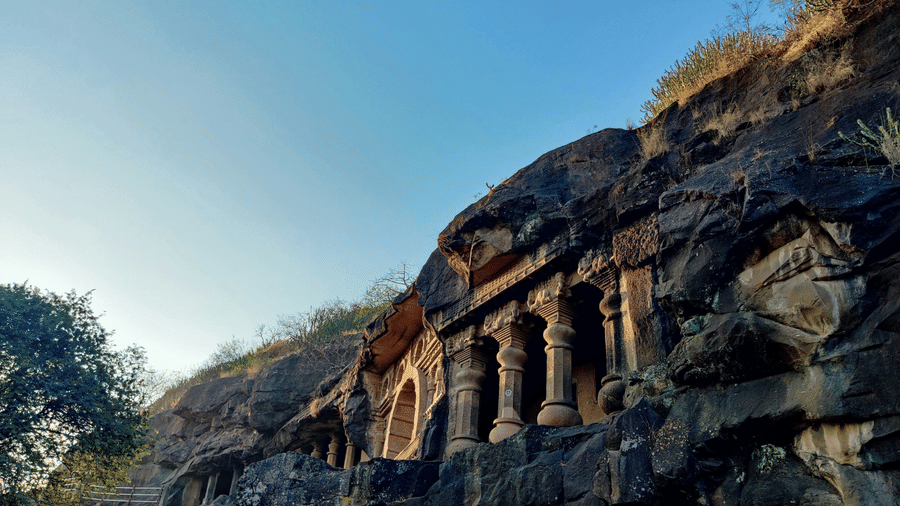A view from below of one of the Pandavleni Caves (Nashik), a 3rd century BCE cave, on the side of a mountain with blue sky in the background.