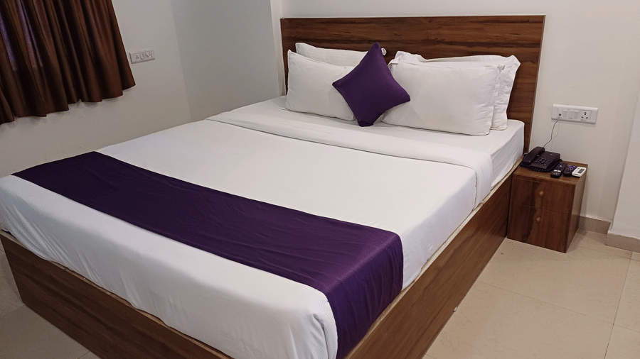 A view of the Deluxe Hotel Rooms in Daman with a side table, a telephone, wall mounted lights, and an AC at VITS Daman Devka Beach.