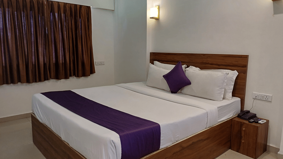 An overview of the Deluxe Room with a side table, a telephone, wall mounted lights, and an AC at VITS Daman Devka Beach. It is the ideal room for the perfect stay in Daman, near the beach.