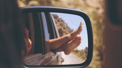 car mirror's side view of a person's feet out the window with nature in the background.