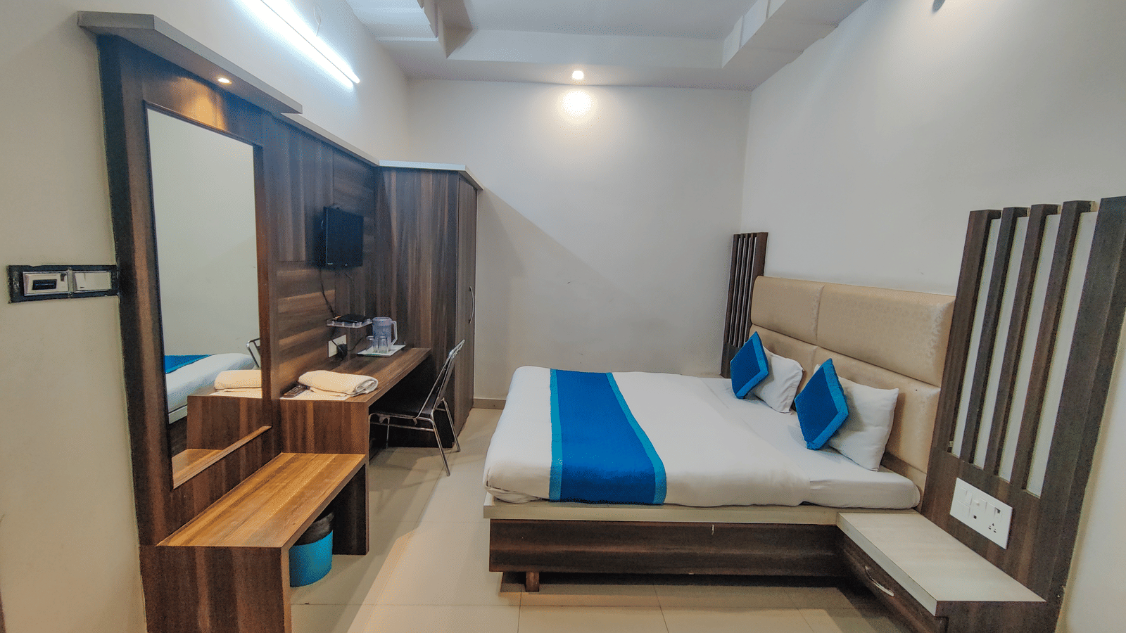 Brightly-lit hotel room featuring a large bed with a blue and white cover, wooden headboard, and a mirrored vanity area - Perfectstayz Value Grey Castle, Haridwar