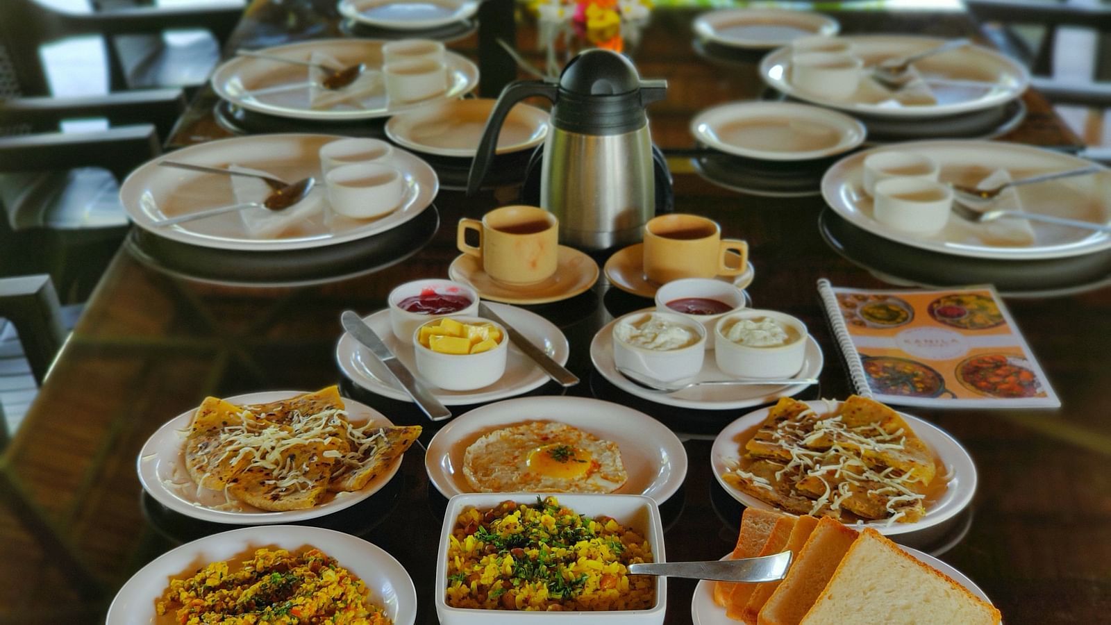 A wooden table is covered with plates of various appetisers. There are french fries, bread, and coffee | The Kanila Resort