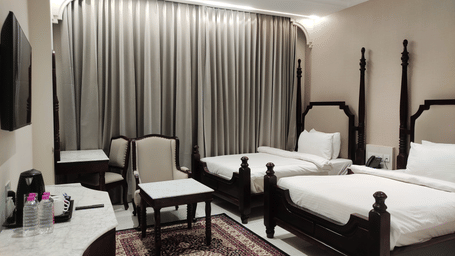A room at Anant Mahal, Jaipur featuring 2 double beds, a patterned rug, a wall mounted television, a dressing table, and 2 cushioned chairs.