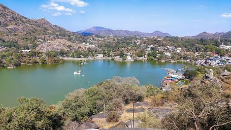 Lake surrounded by hills and trees, a town visible in the distance.