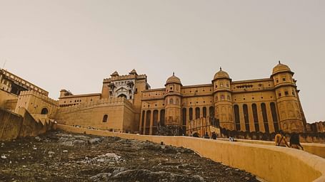 A wide shot of Amber Fort with yellow sandstone walls and ramparts against a pale sky, with a rough foreground