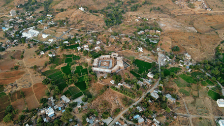 An aerial shot of a small village nestled in a dry, hilly landscape, showing fields and scattered buildings.