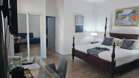 The Junior King Suite at Hotel 39, Jamaica, with a 4-poster bed, a glass-top work desk, a wardrobe, and an open bathroom doorway.