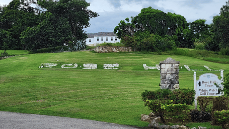 A view of the Rose Hall Great House, Montego Bay, with a lush green lawn in front of it with a signage.