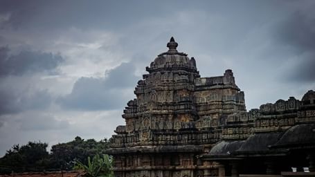 A facade of a Hindu temple under a cloudy sky and trees surrounding it.