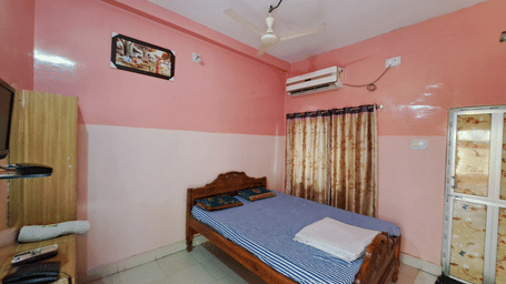 A Semi Deluxe AC Room at Khairi Resorts contains a bed, a ceiling fan, a wall-mounted AC unit, and a corner cupboard.