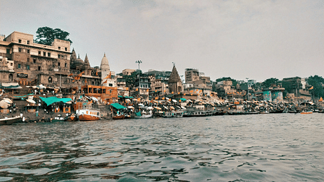 A wide view of Varanasi ghats from the Ganges River with historic buildings in the background.