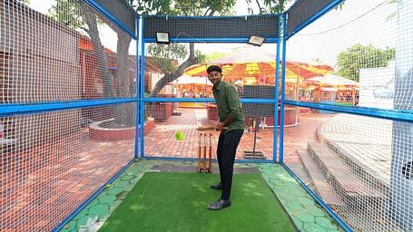 A boy playing cricket in outdoor setting which is covered with nets to prevent cricket ball from going far. 