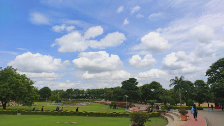 A park pathway with green field by the side, and people passing by.
