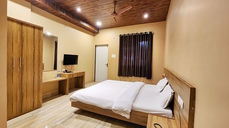 Overview of a Pool View Standard Room at The Kanila Resort with a queen sized bed, a nightstand, a TV, and a desk. 