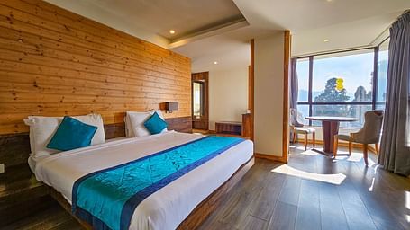 An image of a premium suite with a bed, chair, table, and expansive window overlooking the scenic view - Yashshree Sanderling, Darjeeling