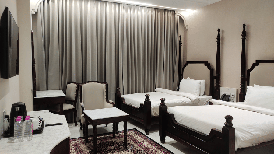 A room at Anant Mahal, Jaipur featuring 2 double beds, a patterned rug, a wall mounted television, a dressing table, and 2 cushioned chairs.