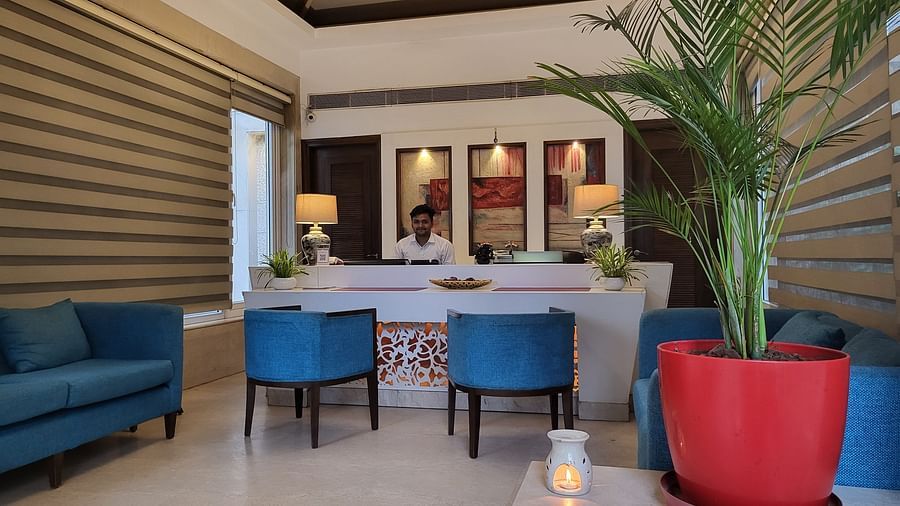 A reception lobby featuring sofas, chairs, reception desk where a receptionist is sitting, and lights hanging from the ceiling - Inde Hotel Signature Tower Gurgaon