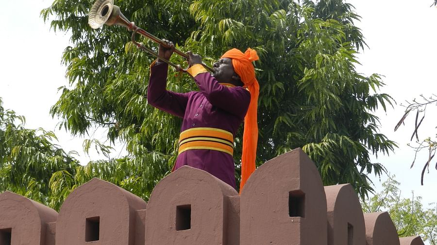 A man in traditional attire playing an instrument atop a fortified wall  - Khas Bagh, Jaipur.