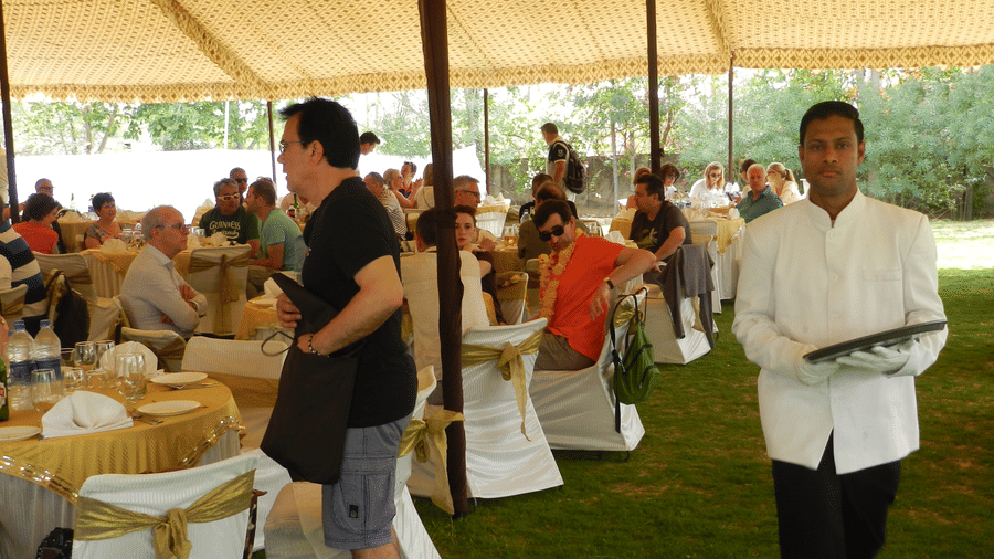 Guests enjoy an open-air meal under a grand canopy, served by courteous staff on lush green lawns - Khas Bagh, Jaipur.