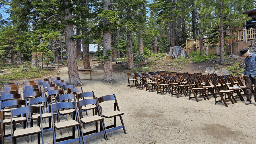An open event setup at Kit Carson Lodge with rows of wooden chairs arranged on a sandy ground amidst a forested backdrop
