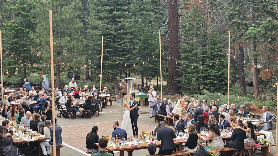An outdoor dining area with numerous guests seated at tables, surrounded by tall pine trees in a wooded setting - Kit Carson Lodge