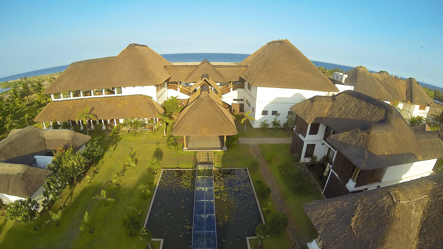 An aerial view looking down at the main thatched-roof resort building, the green gardens, and the central water walkway | Le Pondy