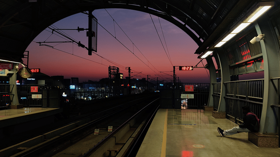 Metro platform at sunset with train tracks and commuters waiting under station lights.