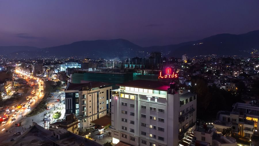 Aerial view of Mandala Norling Lords Prime hotel in Kathmandu at dusk with a hilly landscape in the background a busy road close to the property.