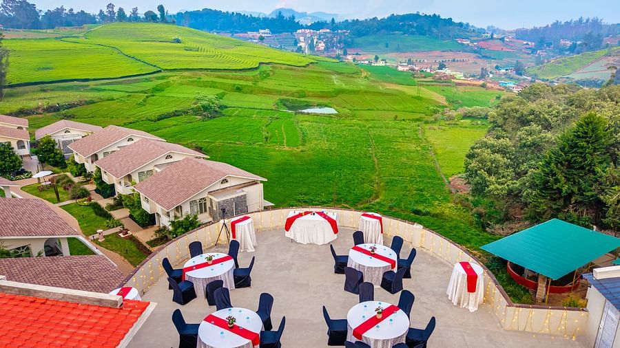 Rooftop event area at Mango Hill Shola, Ooty, viewed from above, with resort staff standing nearby and expansive views of surrounding hills and greenery.