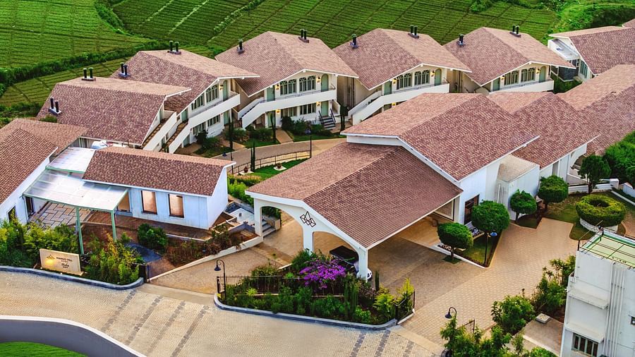 Bird's-eye view of Mango Hill Shola, Ooty, showcasing white buildings with tiled roofs, bordered by trees and a paved pathway through the property.