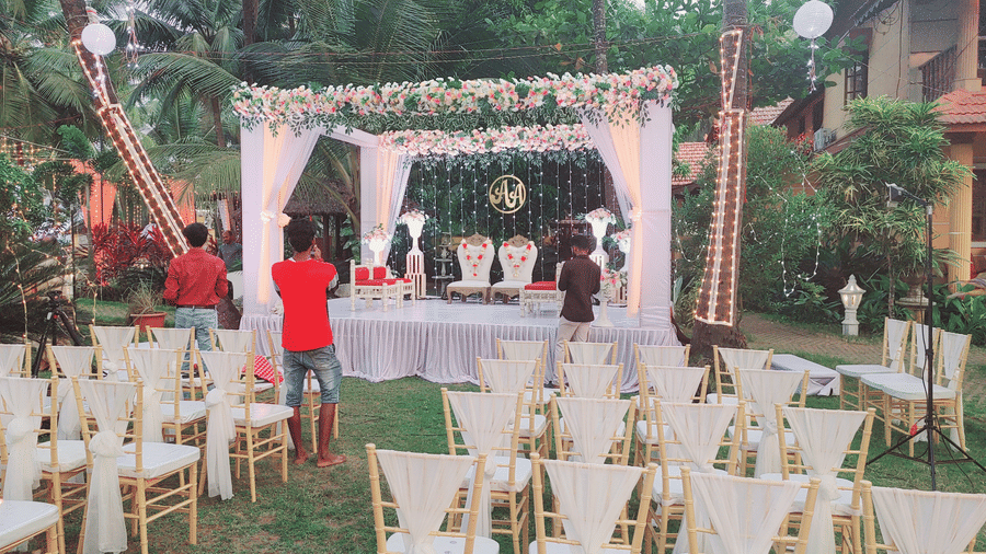 Outdoor wedding setup with white chairs, floral arch, and people arranging decorations at Paradise Lagoon Resort, Udupi.