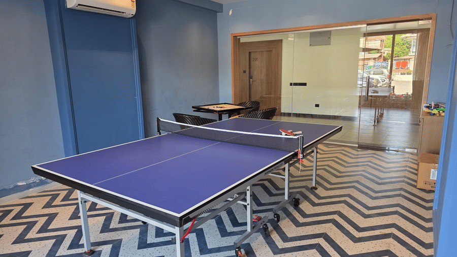 A table tennis table with paddles stands inside a game room with chevron floor tile patterns at Savyasaachii Hotel.