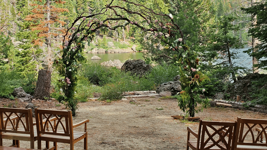 Rustic outdoor wedding ceremony space with wooden chairs and a floral arch in a forest setting at Kit Carson Lodge.
