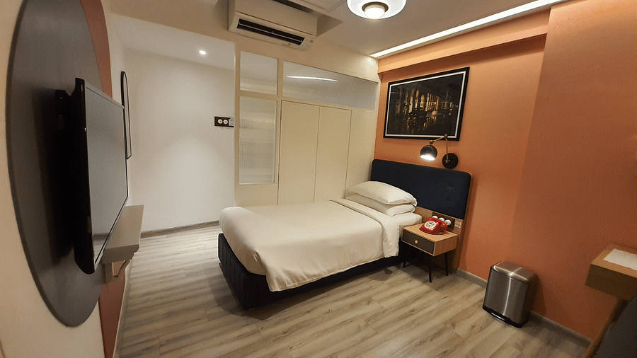 A compact hotel room with a single bed, a small desk, and a flat-screen TV mounted on the wall. The room is decorated in a modern style with orange and white accents.  | T24 Retro