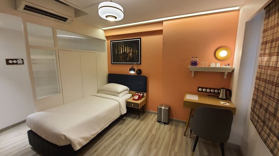 A cosy and well-lit hotel room with a single bed, a bedside table, a wardrobe, a work desk, and a window with curtains   | T24 Retro