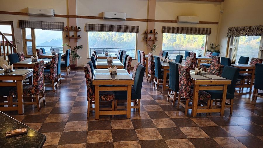 Spacious dining area with wooden furniture and large windows at Dagshai Manor Kasauli - Inde Hotels.