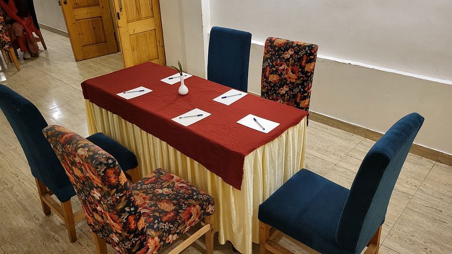 A meeting setup with a table covered in red and gold fabric, surrounded by floral-patterned chairs in a well-lit room at Dagshai Manor Kasauli - Inde Hotels.